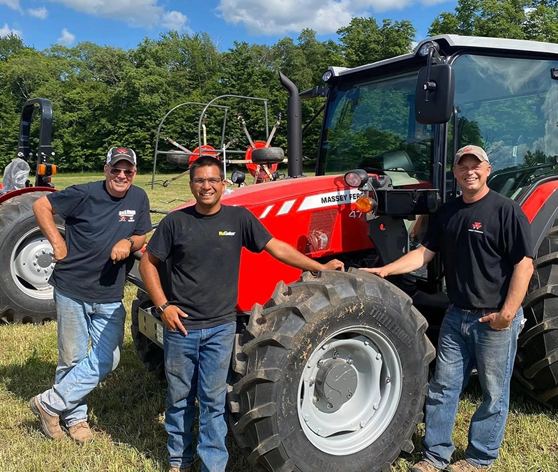 Eklund Farm Machinery team members standing beside a Massey Ferguson tractor in a field in Stamford, NY
