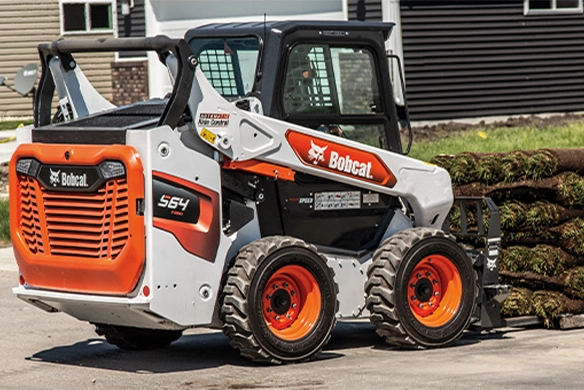 Bobcat S64 skid-steer loader moving sod with a pallet fork attachment, designed for landscaping and material handling tasks.