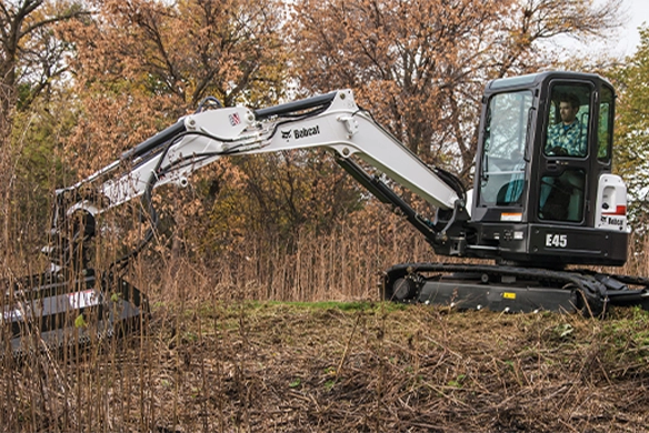 Bobcat E45 compact excavator clearing vegetation with a flail mower attachment, perfect for land maintenance and site prep.