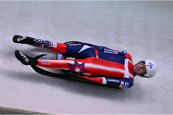 USA Luge athlete in a red, white, and blue suit racing down the icy track during a high-speed competition.