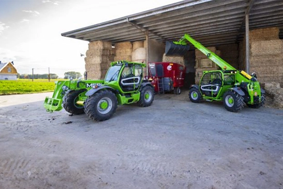 Two Merlo TF30.9 telehandlers operating in a hay storage area, showcasing compact versatility for lifting and loading on farms.