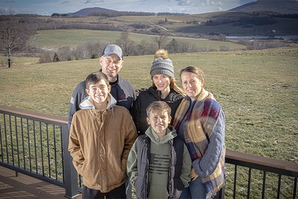The Eklund family smiling outdoors with rolling farmland and hills in the background.